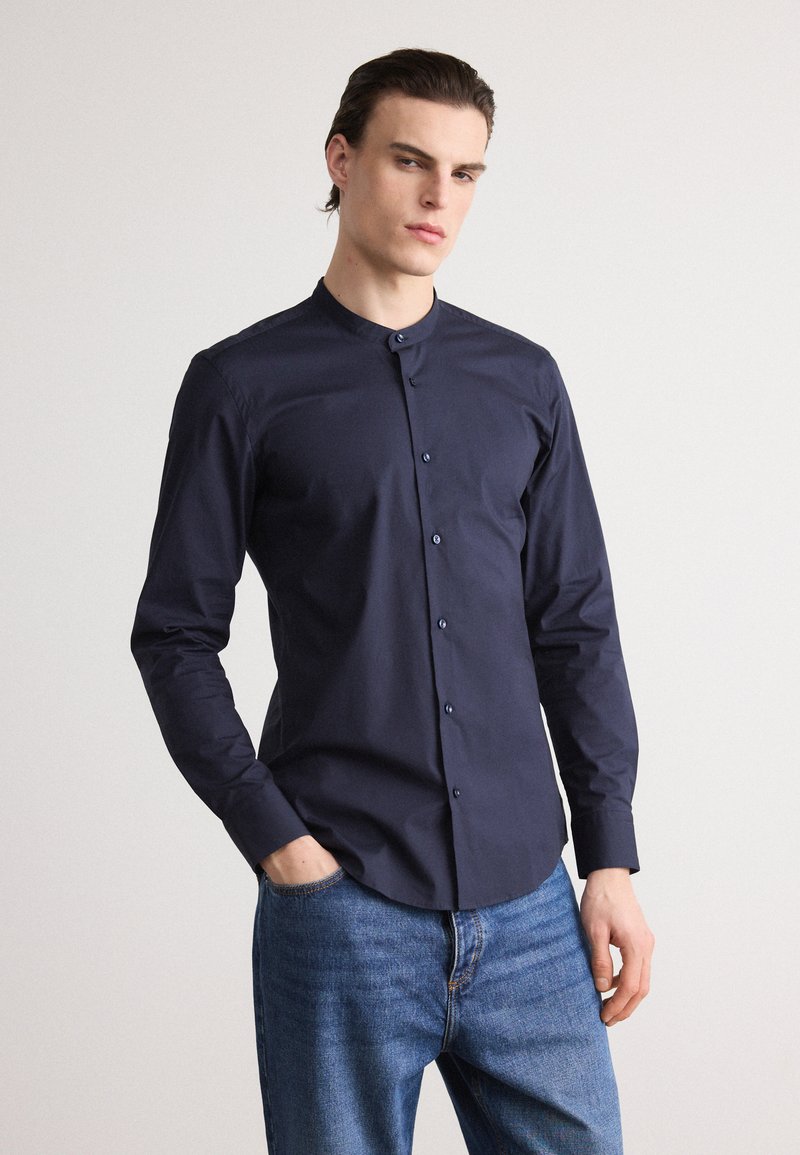 Navy blue, long-sleeve shirt with a round collar and button-down front. Made of smooth fabric, features a slim fit and minimal design.
