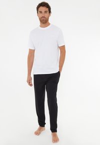Hvid bomulds t-shirt med korte ærmer, parret med sorte, bløde stofbukser med elastisk talje og smalle ben.
