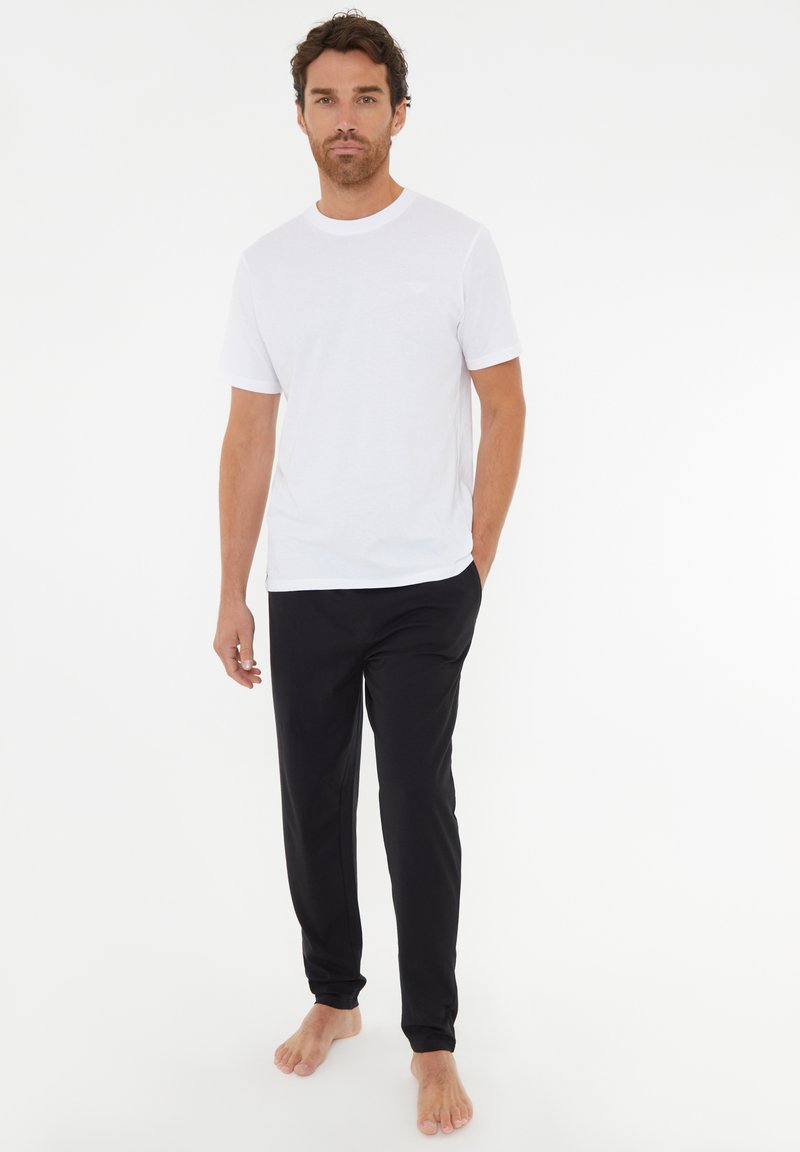 Hvid bomulds t-shirt med korte ærmer, parret med sorte, bløde stofbukser med elastisk talje og smalle ben.