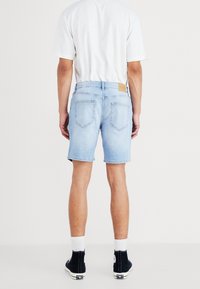 Pantalones cortos de mezclilla azul claros con un corte recto, dobladillos enrollados y dos bolsillos traseros. Combinados con una camiseta blanca y zapatillas altas negras.
