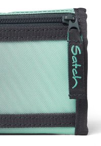 Pochette en tissu vert menthe avec fermeture éclair et bord noir. Présente une étiquette logo bien visible en fil turquoise. Détails de surface texturée visibles.