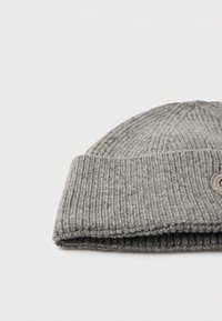 Gorro de punto gris con textura acanalada, con puño doblado y parche circular con logo. Material suave y cálido, adecuado para clima frío.