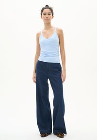 Débardeur bleu clair à côtes avec des bretelles fines, associé à un jean noir en denim à jambes larges présentant une silhouette droite et des coutures contrastées.