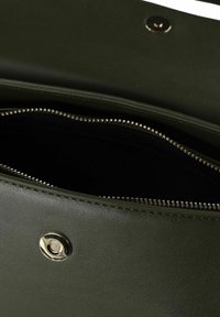 Interior de bolso de cuero verde oscuro con una cremallera plateada brillante, con textura suave y cierre magnético.