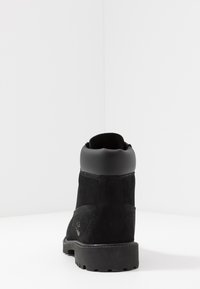 Stivale alla caviglia in suede nero con punta arrotondata, superficie texturizzata e suola in gomma nera. Presenta un colletto imbottito e un dettaglio del logo sul lato.