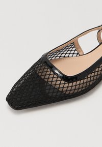 Ballerine en mesh noir avec un bout pointu. Présente une bordure en patin noir brillant le long du bord et une semelle intérieure beige douce.