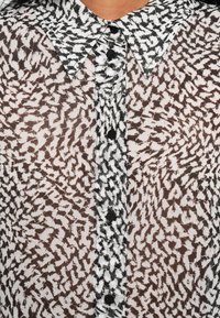 Sheer blouse with a black and white abstract pattern, featuring a collared neckline and button front closure. Lightweight fabric texture.