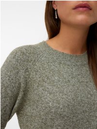 Primo piano di una persona che indossa un maglione a maglia verde e un orecchino di perle pendente, che mostra il collo, la spalla e la parte inferiore del volto.