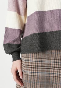 Knitted sweater with horizontal stripes in light purple, cream, and dark gray, featuring ribbed cuffs. Paired with a plaid skirt in brown tones.