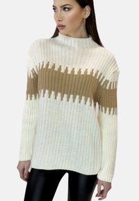Krämfärgad och tanrandig tröja med hög krage och geometrisk design, ihop med svarta, figurnära leggings.