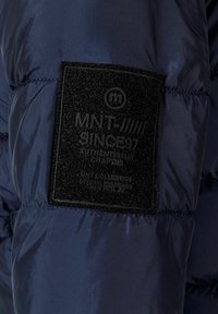 Navy blue puffer jacket fabric with a textured black patch. Patch features embossed branding and details in gray, stitched to the sleeve.
