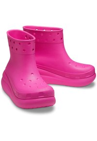 Botas de tobillo de goma de color rosa brillante con un acabado texturizado, orificios de ventilación circulares y una suela gruesa con un patrón de relieve distintivo.
