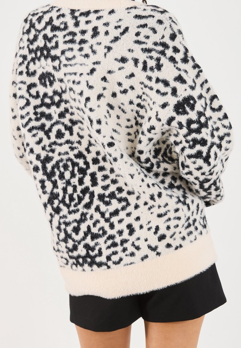 Pull duveteux à motif abstrait noir et blanc porté avec un short noir, vu de dos.
