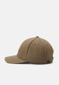 Brun baseball cap med stiv buet skygge og stofmærke på forsiden, set fra venstre side på hvid baggrund.