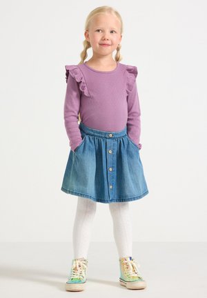 Top lungo viola a maniche ruffle, abbinato a una gonna di jeans con bottoni frontali. Calze bianche a fantasia e sneaker multicolore.