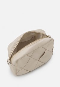 Beige leren tas met rits aan de bovenkant, met een doorgestikt ontwerp, ronde vorm en zilverkleurige hardware. Het interieur heeft een gladde, lichte stofvoering.