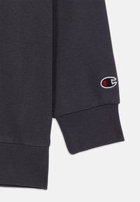 Donkergrijze sweatshirt met ribbelmanchetten, gemaakt van zacht materiaal, met een klein, geborduurd logo met rode en witte accenten op de mouw.