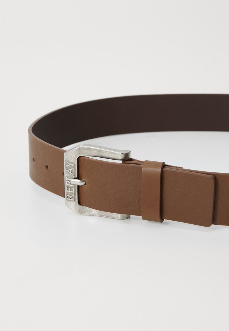 Ceinture en cuir brun avec une boucle en métal argenté portant le nom de marque "REPLAY." Texture lisse avec plusieurs trous d'ajustement.