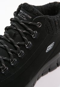 Svarta vandringskängor i mocka och textilmaterial med texturerad krage, metallöglor för snörning och en tjock gummisul för hållbarhet.