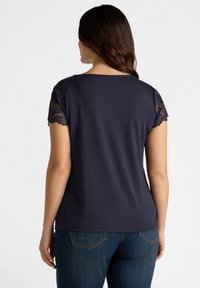 Tricou bleu marin din material moale, cu mâneci scurte din dantelă și decolteu rotund, combinat cu blugi din denim.