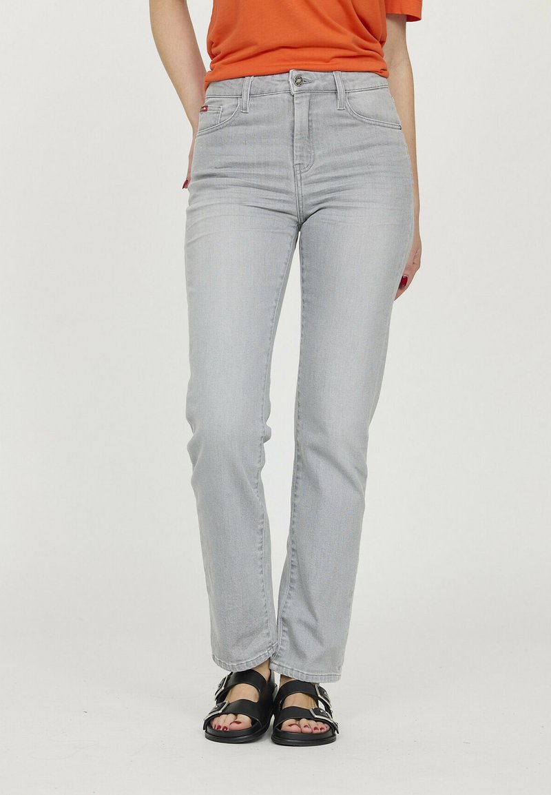 Jean en denim gris avec une coupe slim, taille haute, design à cinq poches et détails de couture subtils. Associés à des sandales noires.