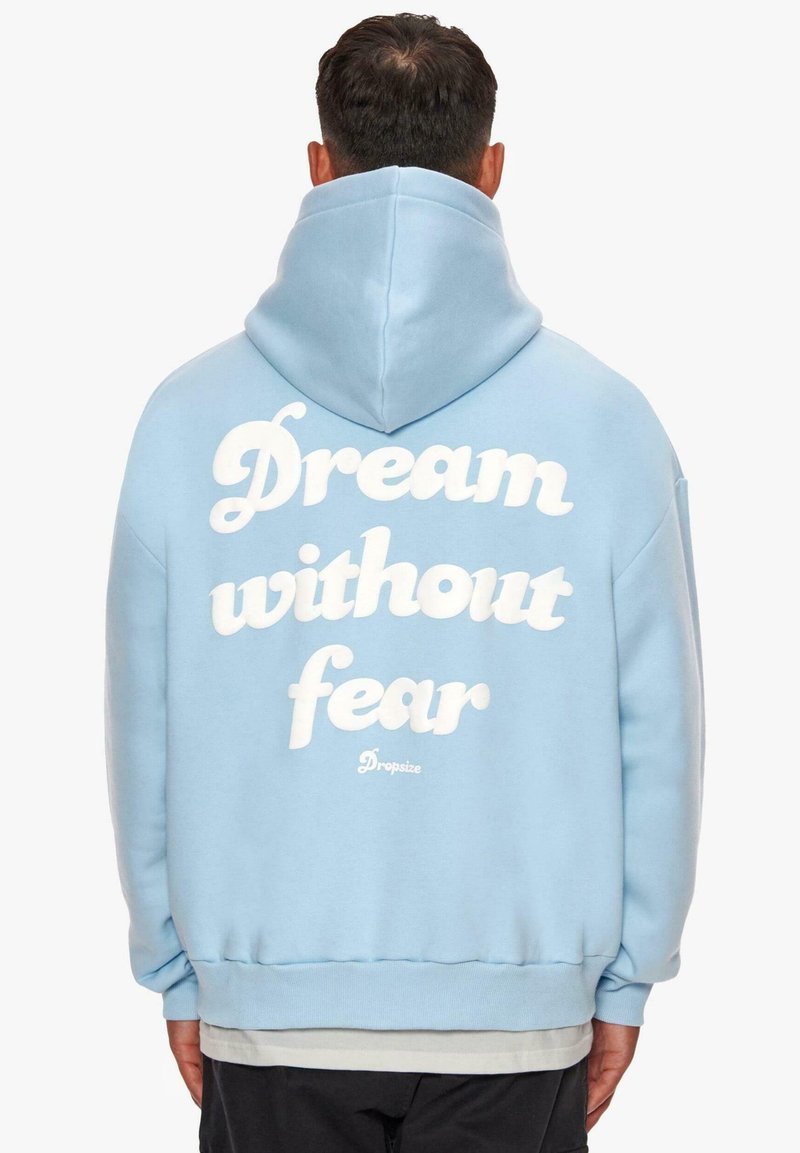 Hellblaue Kapuzenjacke aus weichem Material. Mit auffälligem weißen Text "Träume ohne Angst" auf dem Rücken und einer Kängurutasche vorne.