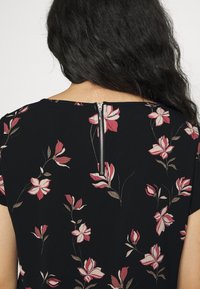Abito nero floreale con fiori rosa e crema. Presenta una cerniera posteriore e maniche corte, realizzato in un tessuto morbido e testurizzato.
