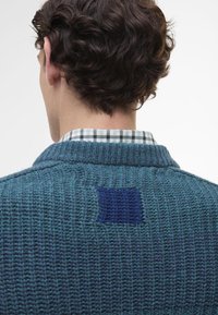 Πλεχτό τιρκουάζ πουλόβερ με υφασμάτινο σχέδιο, που διαθέτει ένα μπλε τονισμένο πάνελ και από κάτω μια καρό πουκάμισο με γιακά.