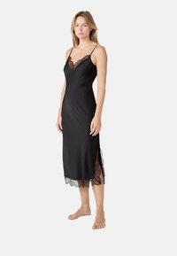 Robe midi en satin noir avec des bretelles fines réglables, un détail en dentelle le long du décolleté et de l'ourlet, ainsi que des fentes sur les côtés pour une touche supplémentaire.