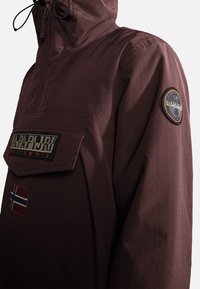 Bordeauxfarbene Pulloverjacke mit Kapuze, ausgestattet mit einer vorderen Pattentasche, Logo-Stickerei und einem angenähten norwegischen Flaggenmotiv. Glatte Textur.