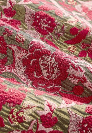 Textile with a floral pattern featuring red and pink flowers on a textured green background, highlighting intricate weaving details.
