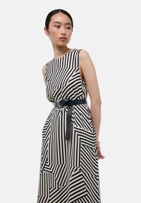 Robe maxi avec un motif à rayures géométriques noir et blanc, sans manches, et une ceinture sombre contrastante à la taille.