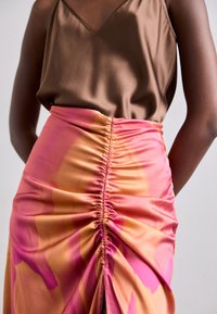 Top en satin brun associé à une jupe à motifs rose et orange, avec des fronces sur le côté pour texture et une silhouette ajustée.
