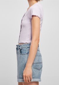 Světlé fialové, žebrované crop top s krátkými, volánkovými rukávy, v kombinaci s vysokými, světlými modrými džíny s ohrnutými lemy.