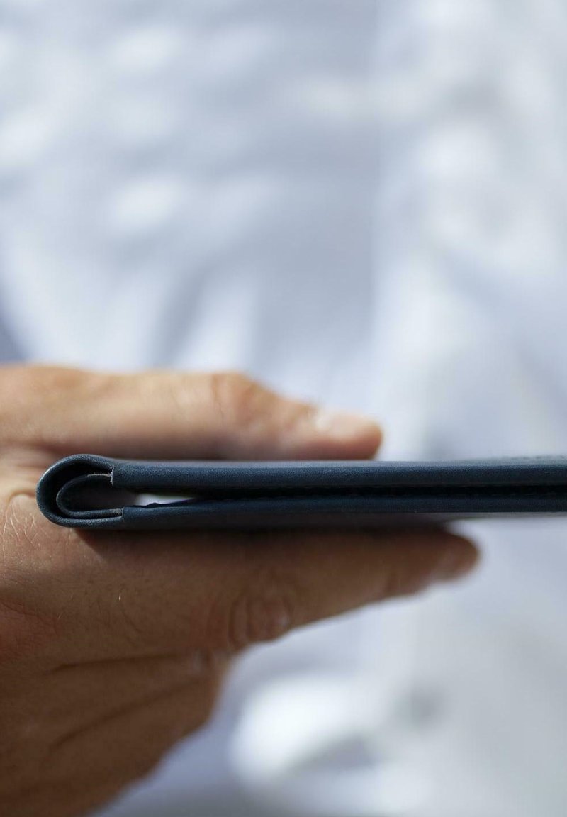 Cuaderno de cuero negro sostenido en una mano, con una textura suave y bordes redondeados, con una costura visible a lo largo del lomo.