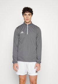Grijze langermige shirt met een ritskraag, voorzien van een wit Adidas-logo op de linkerkant van de borst en elastische manchetten, gecombineerd met witte short.