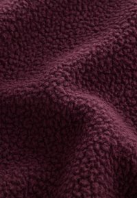 Zamatová, textúrovaná tkanina v hlbokej burgundskej farbe, s jemným, chlpovým povrchom a zdvihnutými, nepravidelnými vzormi po celom povrchu. Ideálna pre teplo.