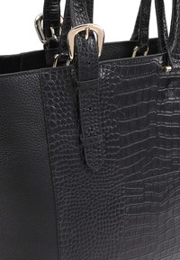 Sac à main noir avec un motif crocodile texturé et du cuir lisse. Il a une forme structurée avec des accessoires en métal doré et des sangles ajustables.