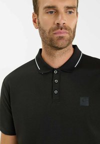 Zwarte poloshirt van gladde stof, met een klassieke kraag, een drieknoopssluiting met gestructureerde knopen en een borstlogo-patch.