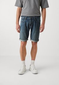 Shorts din denim de un albastru deschis cu manșete răsucite, având cinci buzunare, ușoară uzură și o estompare subtilă, asortate cu adidași albi.