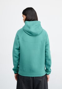 Turquoise hoodie with a large hood, ribbed cuffs, and hem. The fabric appears soft with flatlock seams and a minimalistic design.