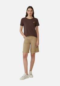 Bruine katoenen t-shirt met een gele banaan grafiek, gecombineerd met beige katoenen shorts en witte veterschoenen. Casual outfit voor warm weer.