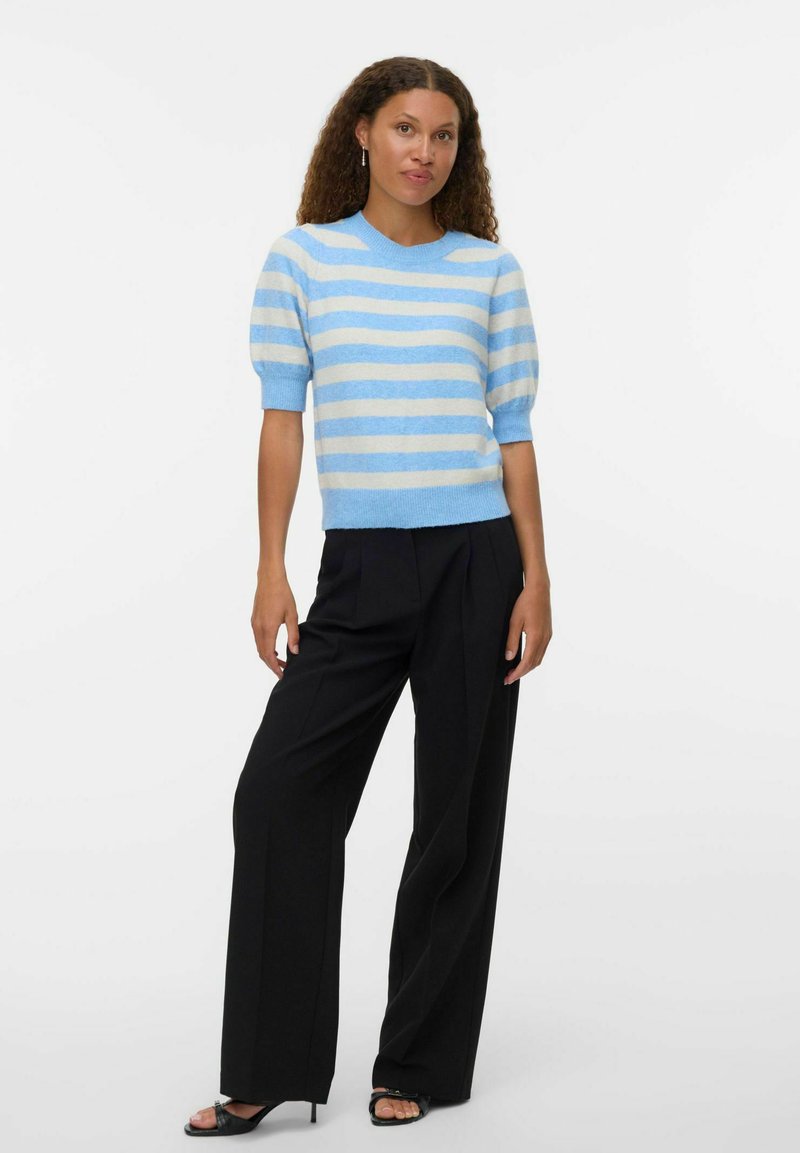 Niebiesko-biała, w prążki, krótko rękawowa sweter z okrągłym dekoltem, zestawiony z czarnymi szerokimi spodniami i czarnymi sandałami na obcasie.