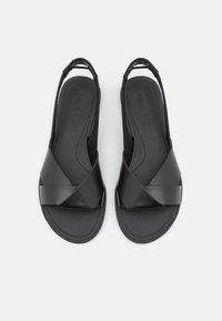 Sandales à bride arrière noires avec un design à bandes croisées, fabriquées en matériau synthétique lisse. Elles disposent d'une semelle intérieure rembourrée et d'une semelle flexible.