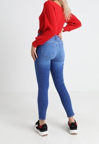 Blå skinny jeans i denim med hög midja och bakfickor, ihopparade med en röd ribbad tröja och svarta sneakers.