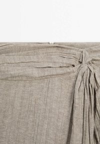 Tissu beige texturé avec des plis verticaux et un détail de nœud noué dans le coin supérieur droit.