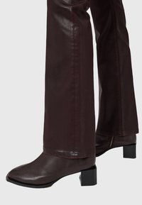 Stivaletti alla caviglia in pelle bordeaux con punta quadrata, tacco basso a blocco e texture liscia. Cuciture visibili e dettagli di zip sul lato.