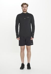 Donkergrijze sporttop met lange mouwen en een kwart rits, gecombineerd met zwart shorts. Bevat subtiele branding en een gestructureerde stof. Zwarte schoenen.