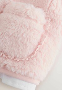 Mīksts rozā siltumizolējošs audums ar teksturētu virsmu, kurai ir viļņa formas malas un balts ribots aproce apakšā.