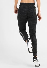 Czarne sportowe spodnie o gładkiej fakturze, dopasowanym kroju i odblaskowych akcentach po bokach. Posiadają zwężane nogawki i elastyczną talię.